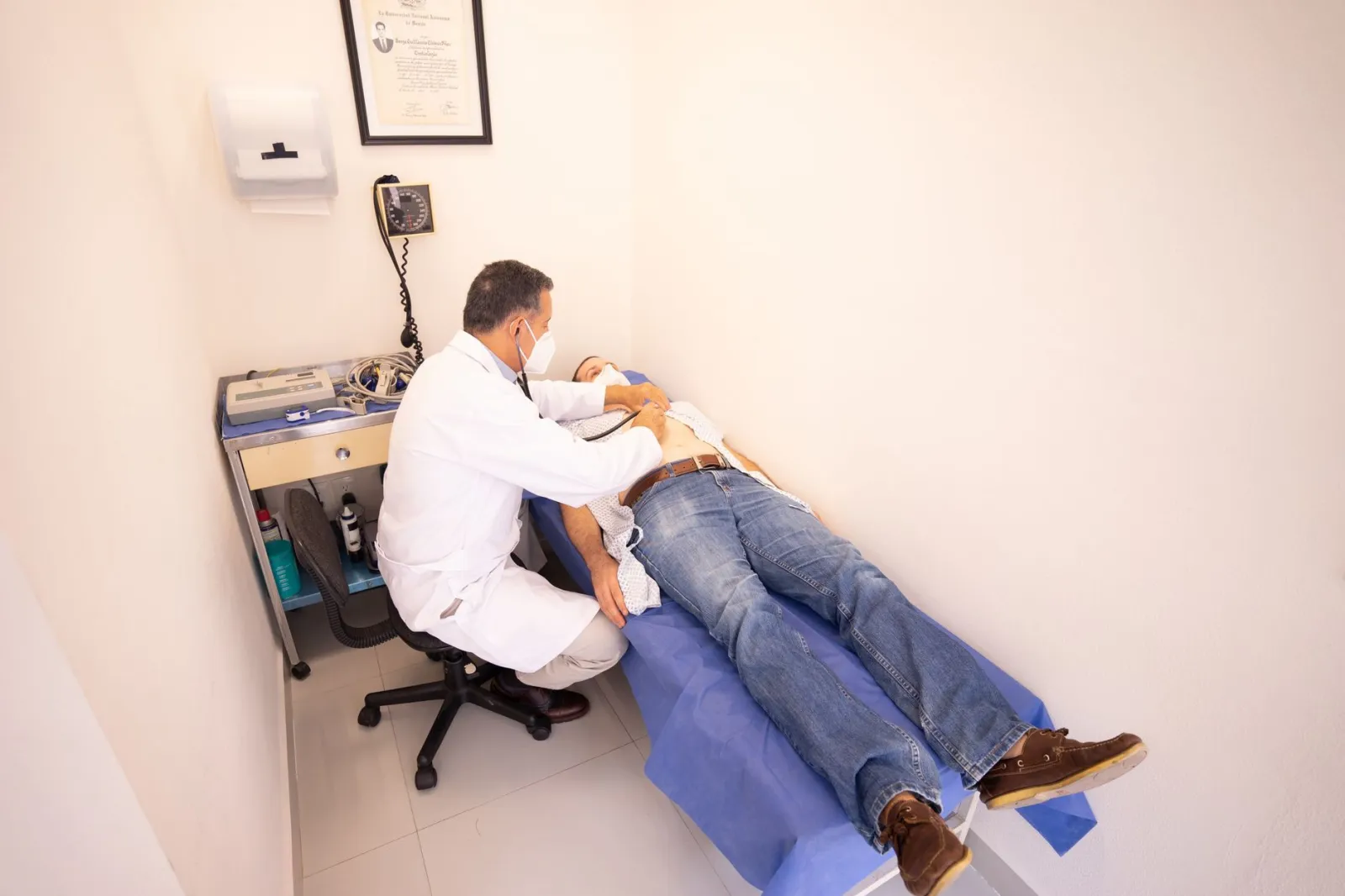 Medical professional examines patient with stethoscope in clinic examination room.